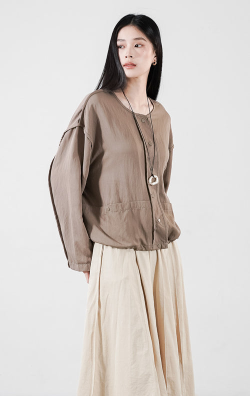 Alexine Jacket kasual warna taupe, jaket ringan dengan detail kancing depan dan tali serut (drawstring), dipadukan dengan rok plisket.