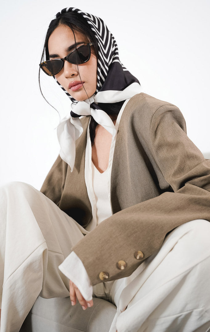 Angeline Blazer warna taupe, blazer open-front berpotongan rapi dengan gaya elegan untuk kerja, dipadukan dengan celana putih.