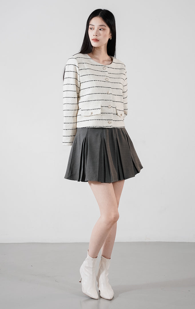 Arianna Top White, blazer crop tweed warna putih dengan motif garis horizontal hitam dan kancing elegan, dipadukan dengan rok plisket.