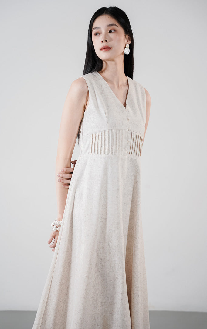 Aurynn Dress warna ivory, gaun midi A-line tanpa lengan berbahan katun dengan detail pintuck di dada, dipadukan dengan sandal hak putih.