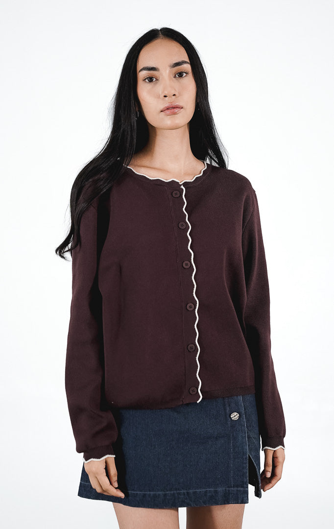 Belucci Cardigan warna dark brown, kardigan rajut lengan panjang dengan detail trim putih bergelombang di tepiannya, dipadukan dengan rok mini denim.