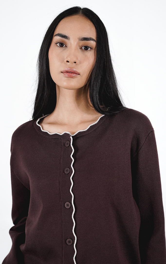 Belucci Cardigan warna dark brown, kardigan rajut lengan panjang dengan detail trim putih bergelombang di tepiannya, dipadukan dengan rok mini denim.