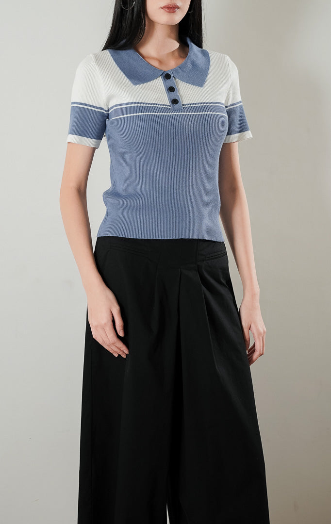 Atasan rajut lengan pendek berkerah Carmen Top bergaya dua warna putih dan dusty blue dengan detail kancing depan, dipadukan dengan celana kulot panjang berwarna hitam.