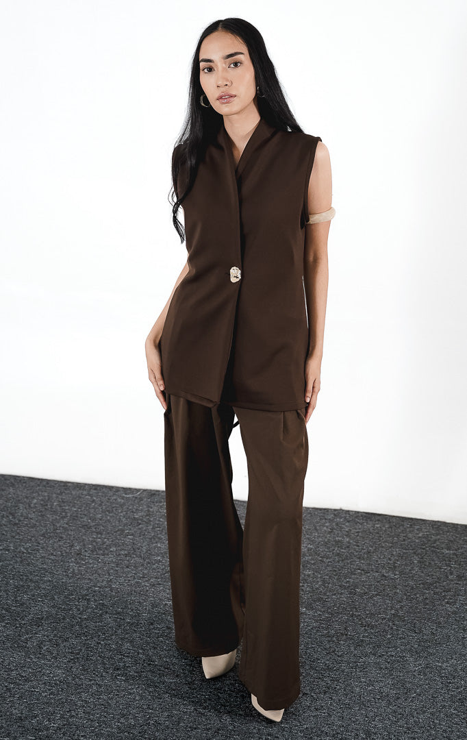 Clyde Vest warna cokelat (brown), rompi panjang tanpa lengan dengan kancing asimetris unik dan kerah V-neck, dipadukan dengan celana panjang senada.