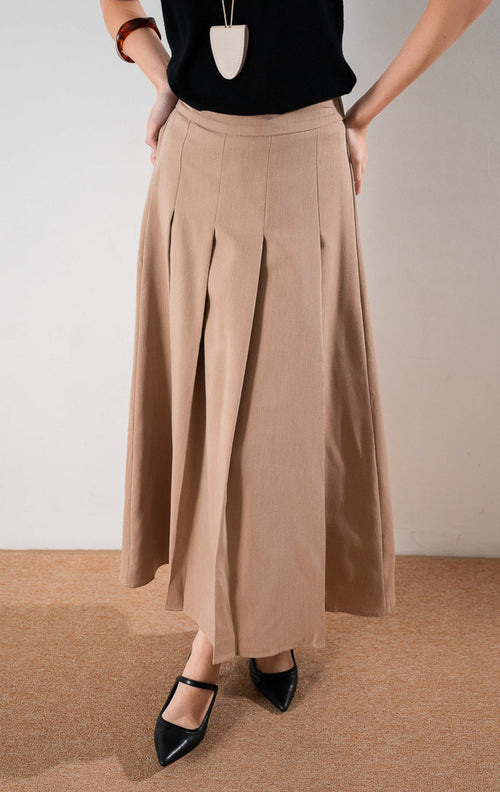 Darana Skirt Brown, rok panjang A line warna cokelat dengan detail lipit (pleats) depan yang rapi, dipadukan dengan tank top hitam dan sepatu hak tinggi hitam.