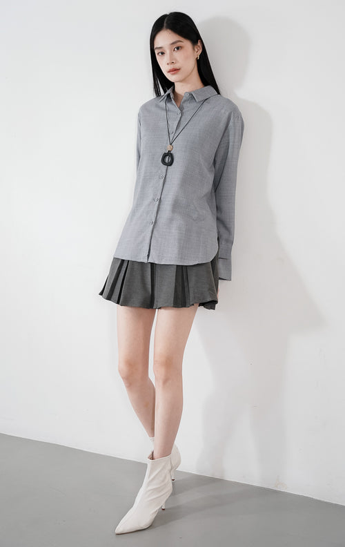 Fabienne Top warna grey, kemeja katun slub lengan panjang dengan kerah klasik dan kancing depan, dipadukan dengan rok plisket abu-abu.