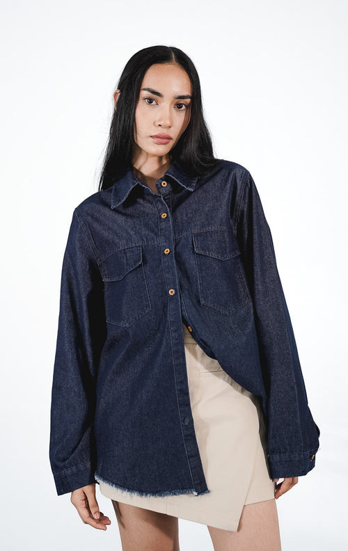 erve Top warna dark denim, kemeja jeans lengan panjang dengan dua saku dada dan ujung bawah rawis (frayed hem), dipadukan dengan rok mini krem.