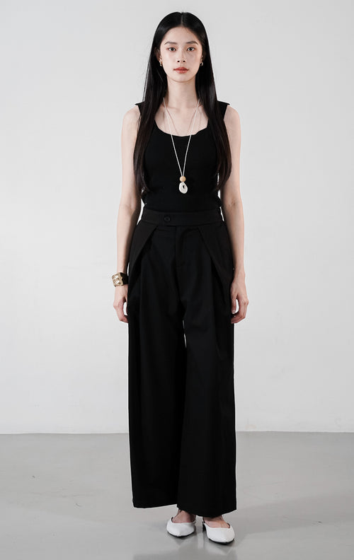Jelson Pants warna hitam, celana panjang wide-leg berpotongan lebar dengan detail panel lipatan besar di depan, dipadukan dengan tank top hitam.