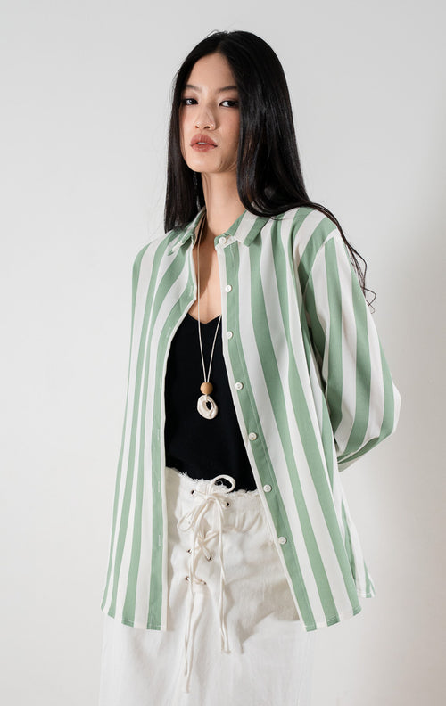 Kemeja lengan panjang motif garis vertikal hijau dan putih Kyoto Top berbahan ringan sebagai luaran atau outer, dipadukan dengan tank top hitam di bagian dalam dan rok panjang berwarna putih