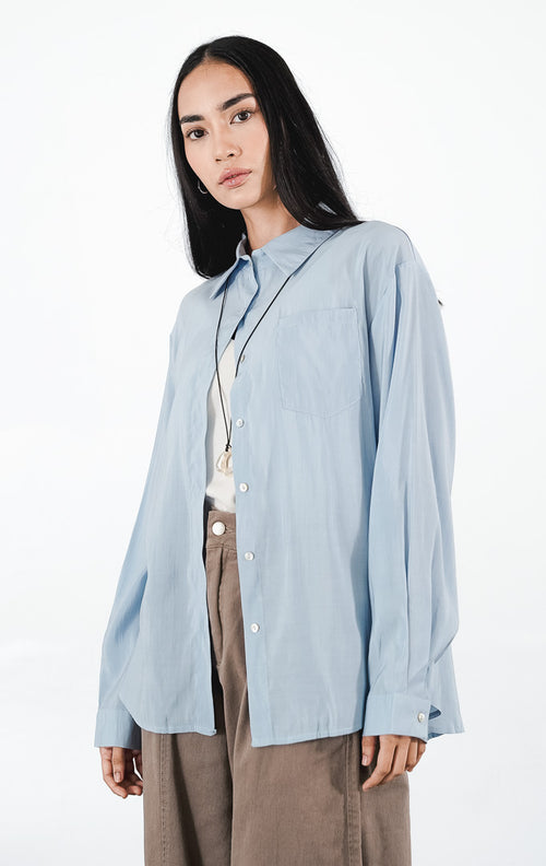 Matea Top warna sky blue, kemeja katun lengan panjang siluet oversized dengan saku dada kiri dan kancing putih minimalis.