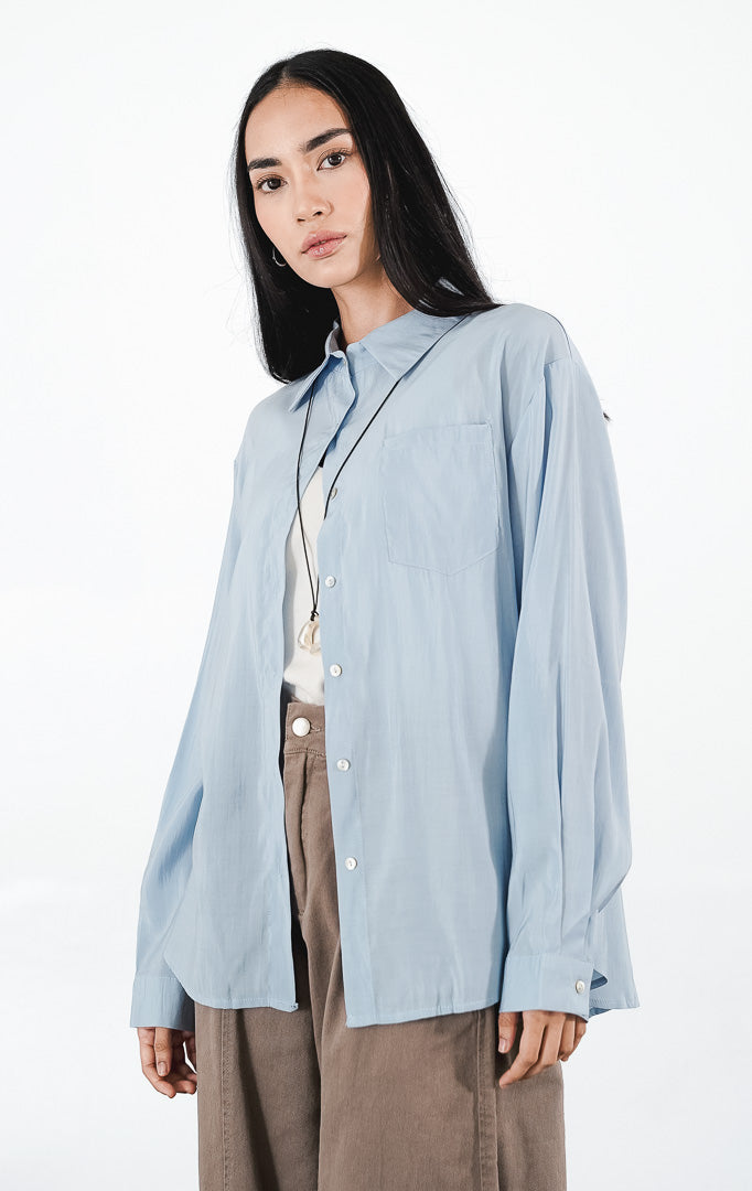Matea Top warna sky blue, kemeja katun lengan panjang siluet oversized dengan saku dada kiri dan kancing putih minimalis.