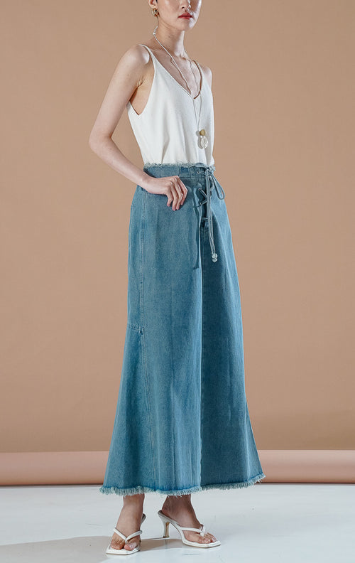 Miller Skirt dengan detail tali serut di bagian depan dan ujung bawah rawis, dipadukan dengan tank top putih.