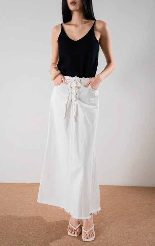 Rok denim panjang berwarna putih Miller Skirt dengan detail tali serut di depan dan ujung bawah rawis, dipadukan dengan tank top hitam.