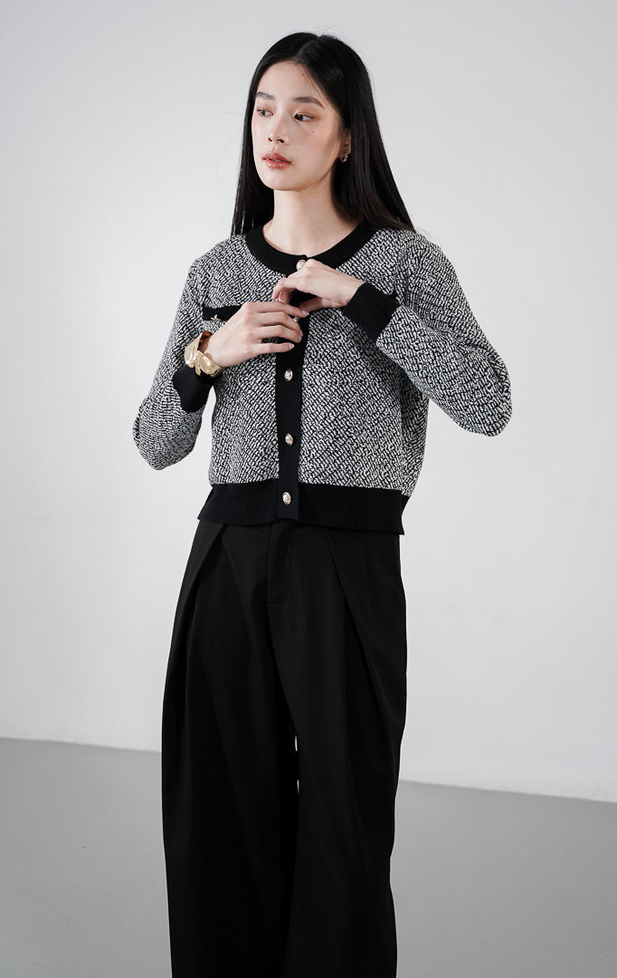 Model mengenakan Monique Cardigan warna black, kardigan rajut pola dua warna dengan detail garis hitam kontras, dua saku dada, dan kancing emas bulat di bagian depan.