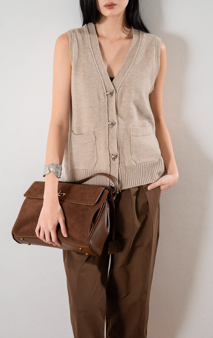 Valeria Vest Khaki, rompi rajut tanpa lengan warna khaki dengan kancing perak dan dua saku depan, dipadukan dengan celana cokelat.