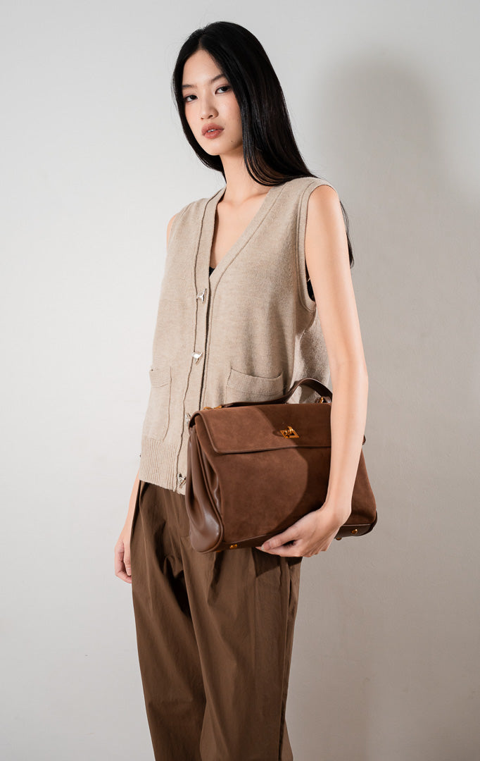 Valeria Vest Khaki, rompi rajut tanpa lengan warna khaki dengan kancing perak dan dua saku depan, dipadukan dengan celana cokelat.