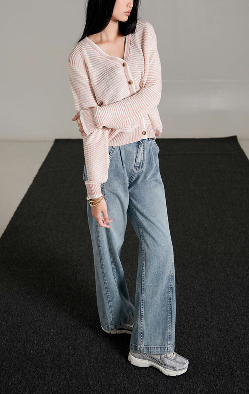 Tampak depan model wanita mengenakan Aderyn Two-Tone Knit Cardigan warna pink dengan kerah v-neck dan kancing depan, dipadukan dengan celana jeans longgar.