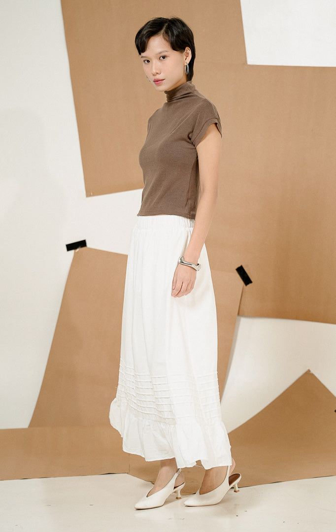 Model mengenakan Adonis Pintuck Ruffles Maxi Skirt White, produk rok panjang putih wanita dengan detail pintuck dan ruffles anggun, dipadukan dengan atasan cokelat.