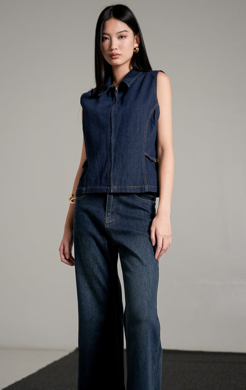 Alice Vest Indigo, sebuah rompi denim tanpa lengan berwarna biru dongker dengan kerah, dipadukan dengan celana jeans panjang senada.