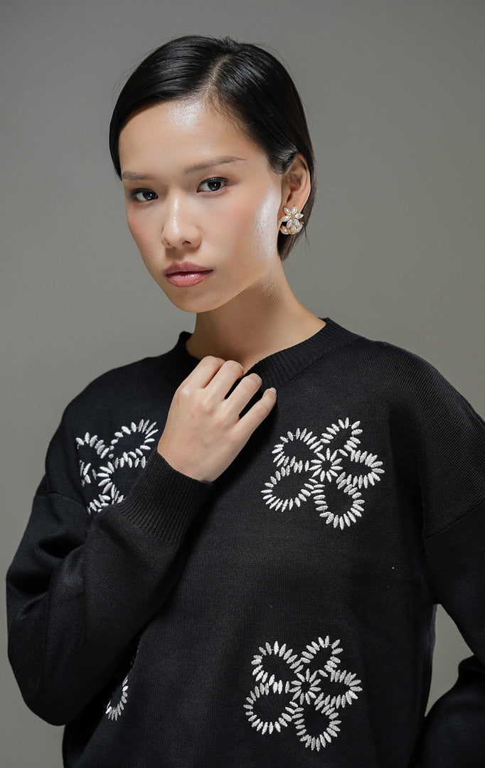Sweater rajut wanita Amora Sweater warna hitam lengan panjang dengan motif bordir bunga besar, kerah bulat, dan detail ribbed hem.