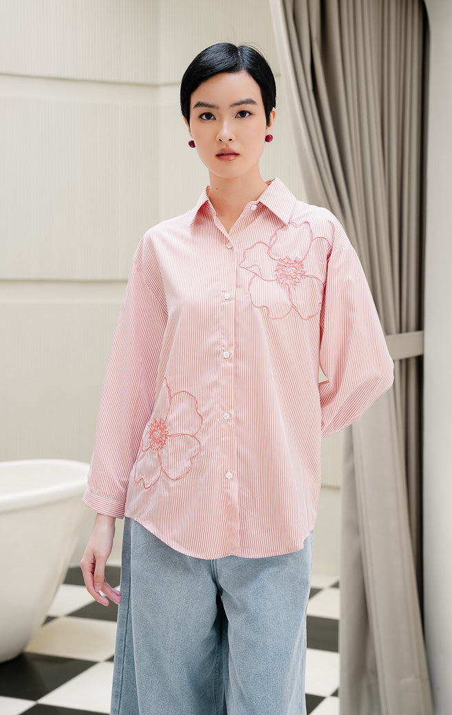 Kemeja lengan panjang wanita Amour Top warna pink peach bermotif stripe (salur) dengan detail bordir bunga (floral embroidery) dan kancing depan.