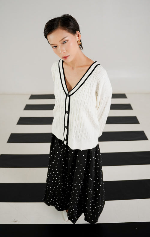 Kardigan rajut wanita Annette White dengan pola cable knit (kepang), kerah V neck bergaris hitam, dan kancing depan hitam dari This Is April.