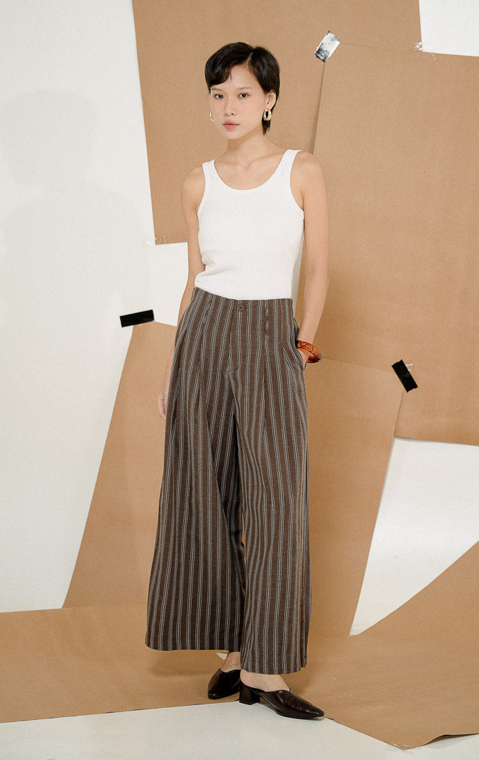 Model berdiri mengenakan Ariphron Striped Culotte Pants Brown, celana kulot wanita motif garis vertikal warna cokelat berbahan katun, dipadukan tank top putih.