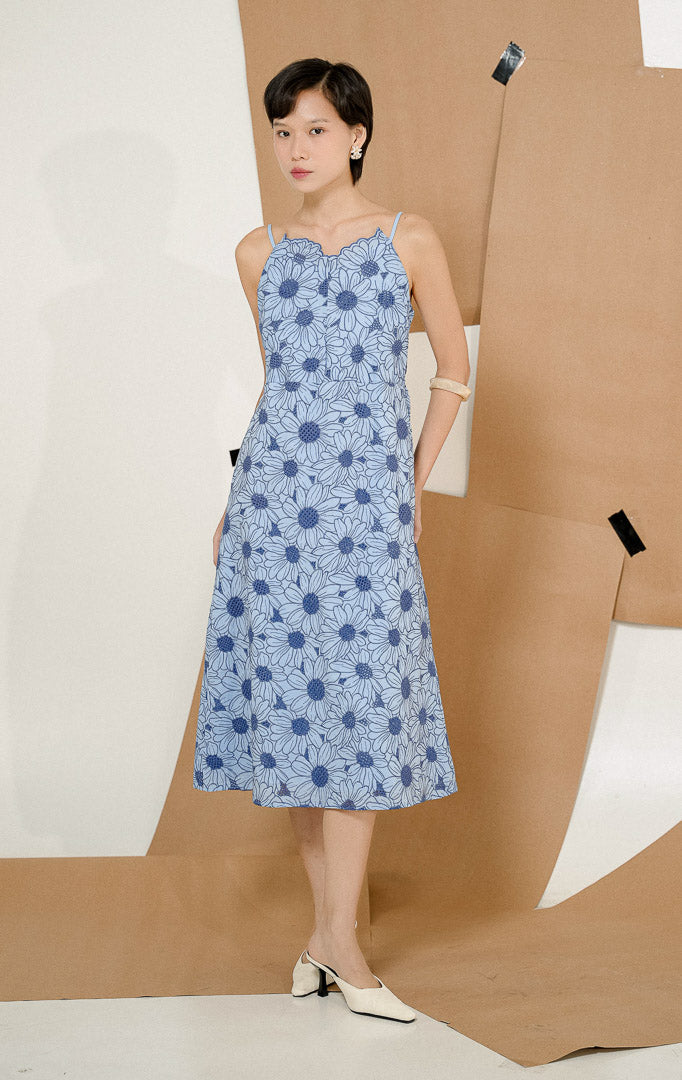 Model berdiri mengenakan Aristelle Bloom Maxi Dress Blue, produk long dress wanita tanpa lengan warna biru dengan detail bordir motif bunga yang anggun.