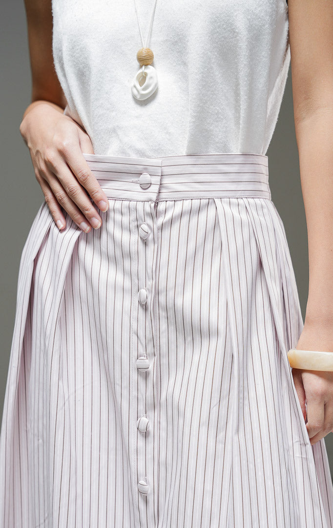 Rok midi wanita Artemis Skirt warna light pink merah muda lembut motif salur garis vertikal dengan kancing depan berlaput kain, detail pleat, dan pinggang karet.