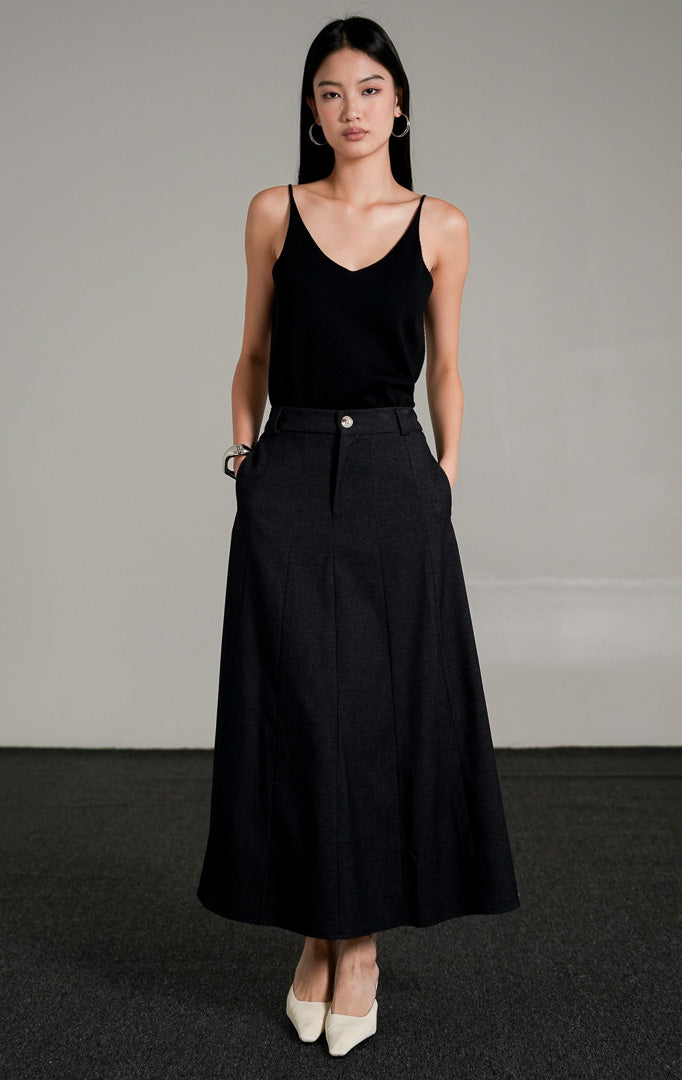 Ashton A-line Skirt berwarna dark denim dengan kancing depan, dipadukan dengan atasan tank top hitam dan sepatu heels putih.