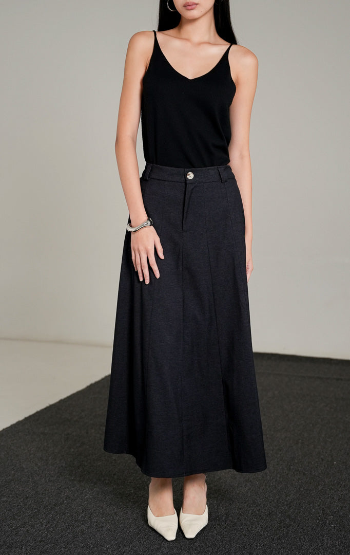 Ashton A-line Skirt berwarna dark denim dengan kancing depan, dipadukan dengan atasan tank top hitam dan sepatu heels putih.