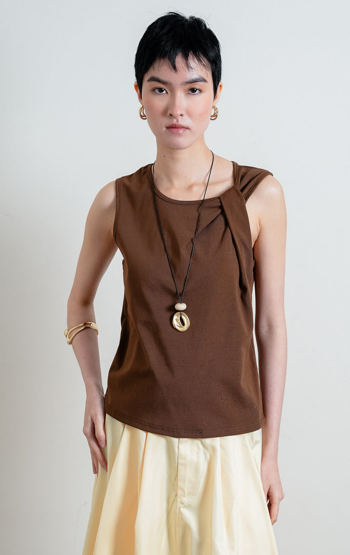 Atasan wanita tanpa lengan warna cokelat (brown sleeveless top) Aspen Top berbahan kain jersey lembut dan halus (soft, smooth jersey fabric) dengan kerah bulat (rounded neckline) dan detail aksen simpul kain di bagian depan (statement tie detail).