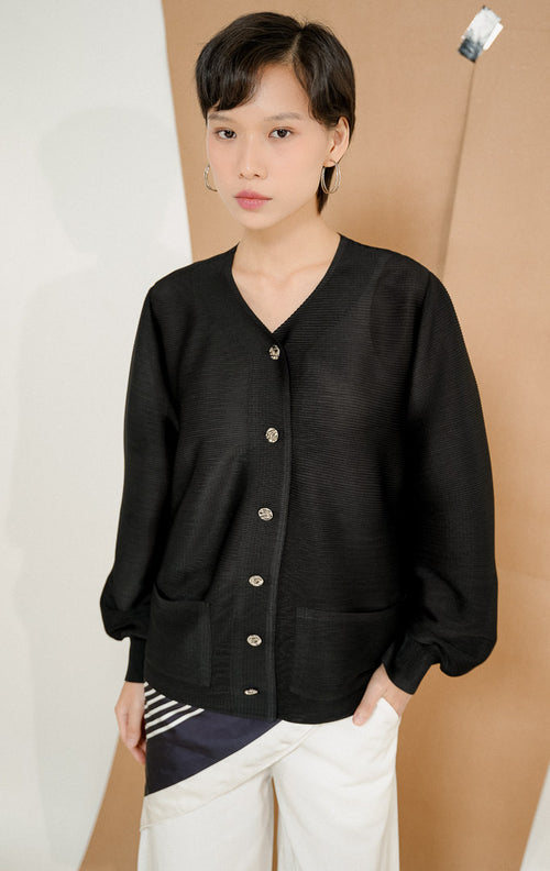 Model berdiri mengenakan Astoria Accordion Pleats Button-Up Top Black, atasan kemeja plisket wanita lengan panjang warna hitam dengan detail kancing silver