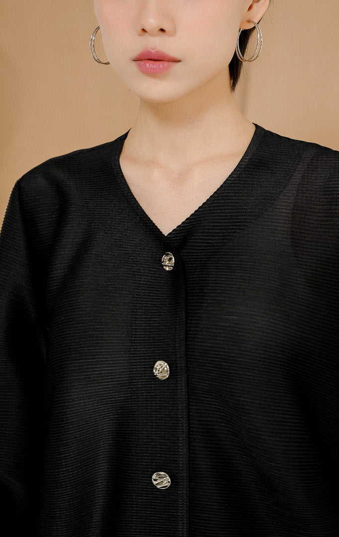 Model berdiri mengenakan Astoria Accordion Pleats Button-Up Top Black, atasan kemeja plisket wanita lengan panjang warna hitam dengan detail kancing silver