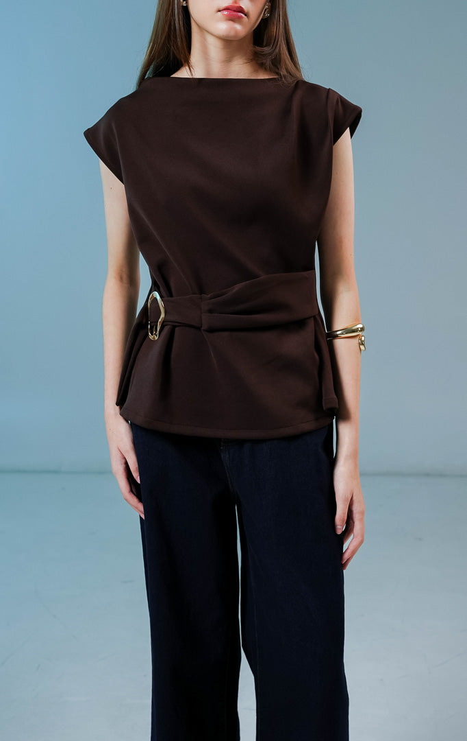 Model wanita mengenakan Carpenter Sleeveless Draped Top warna coklat tua, atasan tanpa lengan berbahan katun poliester dengan siluet drape asimetris dan detail sabuk bergesper di pinggang.