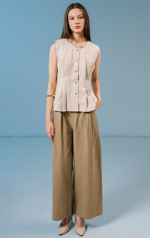 Model wanita mengenakan Cornelia Pleats Sleeveless Top warna khaki, atasan tanpa lengan berbahan katun dengan detail lipit (pleats) yang elegan dan kancing depan.
