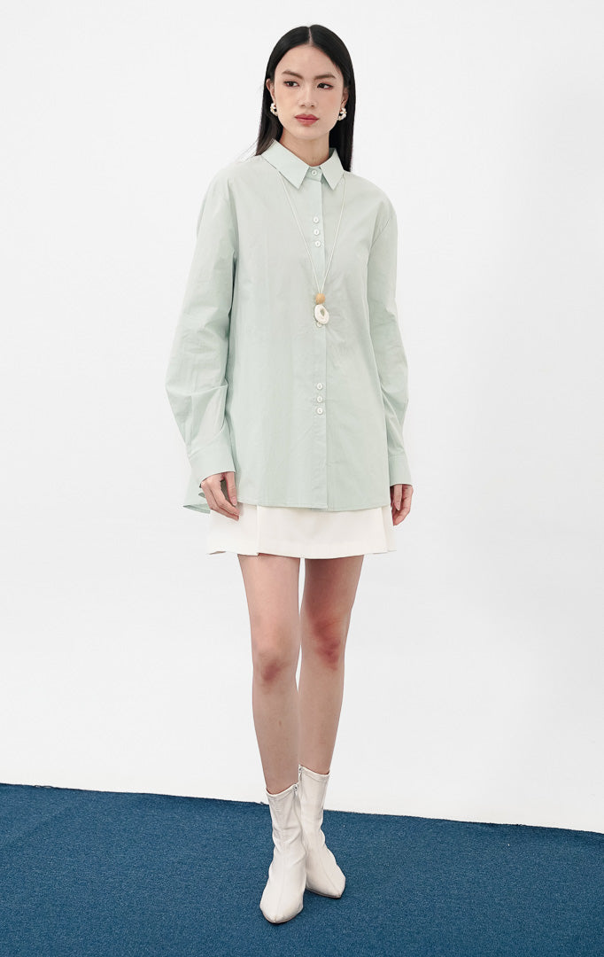 Model mengenakan Athena Top warna sage, kemeja katun lengan panjang siluet oversized dengan kancing depan dan kerah klasik, dipadukan dengan celana denim lebar.