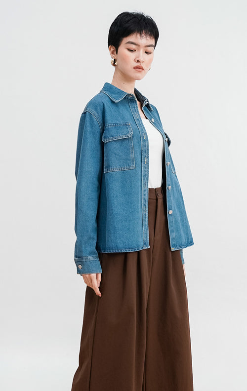 Model mengenakan Ayven Denim Jacket, jaket jeans biru lengan panjang dengan dua saku dada, kancing perak, dan siluet terstruktur yang dipadukan dengan celana cokelat.