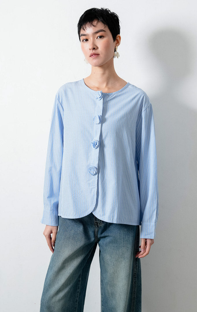 Blus wanita lengan panjang motif garis-garis biru (blue vertical stripes) Azzuria Top dengan kerah bulat (round neckline), detail kancing bungkus berbentuk bunga (floral-shaped fabric-covered buttons), dan kelim melengkung (curved hem).