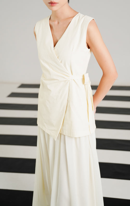 Gaun pesta wanita Barenia Dress Ivory model tanpa lengan (sleeveless), kerah V neck, detail wrap asimetris dengan tali pinggang samping.
