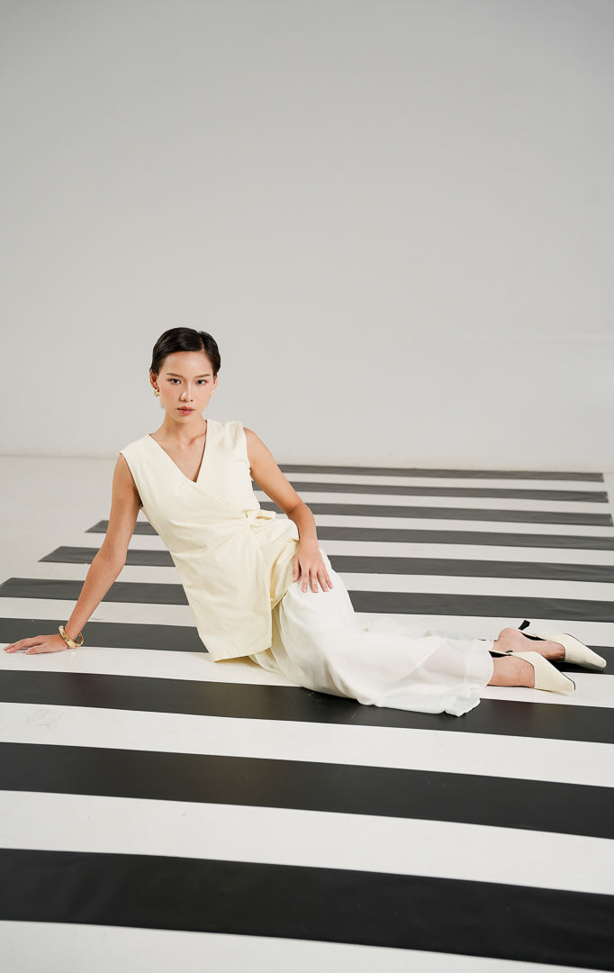Gaun pesta wanita Barenia Dress Ivory model tanpa lengan (sleeveless), kerah V neck, detail wrap asimetris dengan tali pinggang samping.