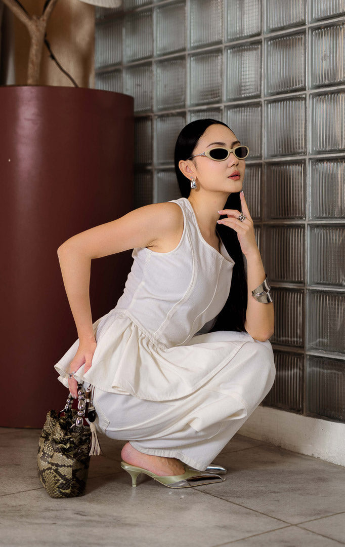 Blouse denim wanita warna putih (white denim peplum blouse) Emalyne Top dengan siluet feminin terstruktur (polished feminine silhouette), potongan pinggang turun yang tegas (defined drop-waist), peplum mengembang lembut (softly flared peplum), dan ritsleting belakang (back-zip closure).