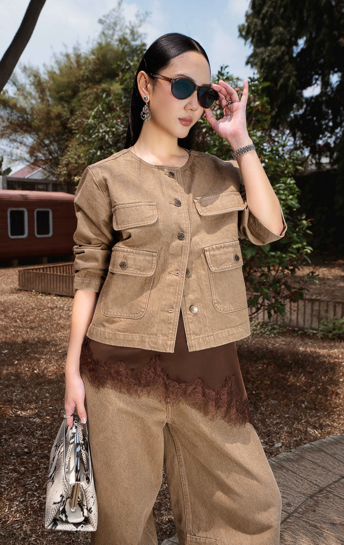 Jaket denim wanita warna cokelat (brown utility denim jacket) Solryn Jacket bahan denim terstruktur non-regang (non-stretch denim), kerah bulat, saku depan fungsional bertingkat (dual-tier functional front pockets), dan penutup kancing depan.