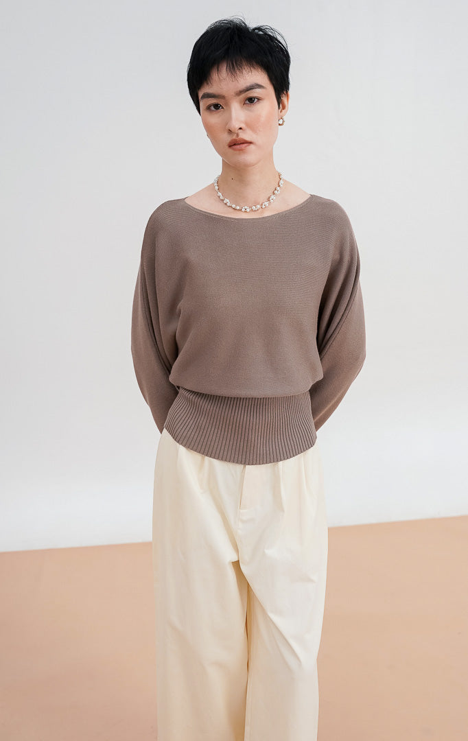 Model mengenakan Blair Sweater warna taupe, atasan rajut lengan panjang dengan potongan leher boat neck dan detail ban pinggang rajut lebar (ribbed waistband).