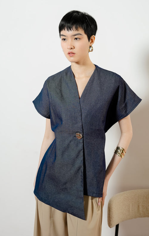 Model wanita mengenakan Loura Minimalist Tailored V-Neck Vest warna navy, atasan blouse wanita lengan pendek berwarna biru dongker dengan potongan asimetris dan kancing logam dekoratif.