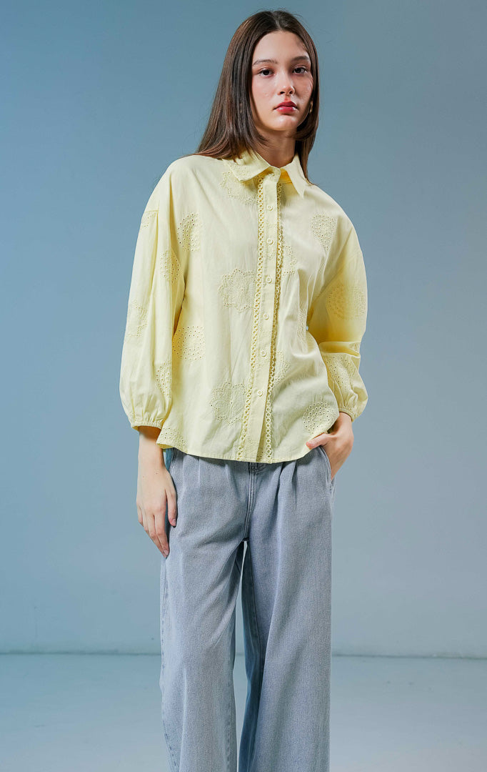 Model wanita mengenakan blouse Dimitry Embroidered Top warna butter yellow, kemeja katun wanita berkerah klasik dengan detail kancing depan dan bordir eyelet yang feminin.