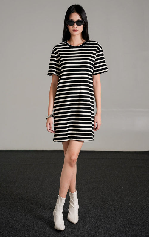 Breezy Striped Knit Dress, sebuah t-shirt dress pendek lengan pendek bermotif garis horizontal hitam dan putih, dipadukan dengan sepatu boots putih.