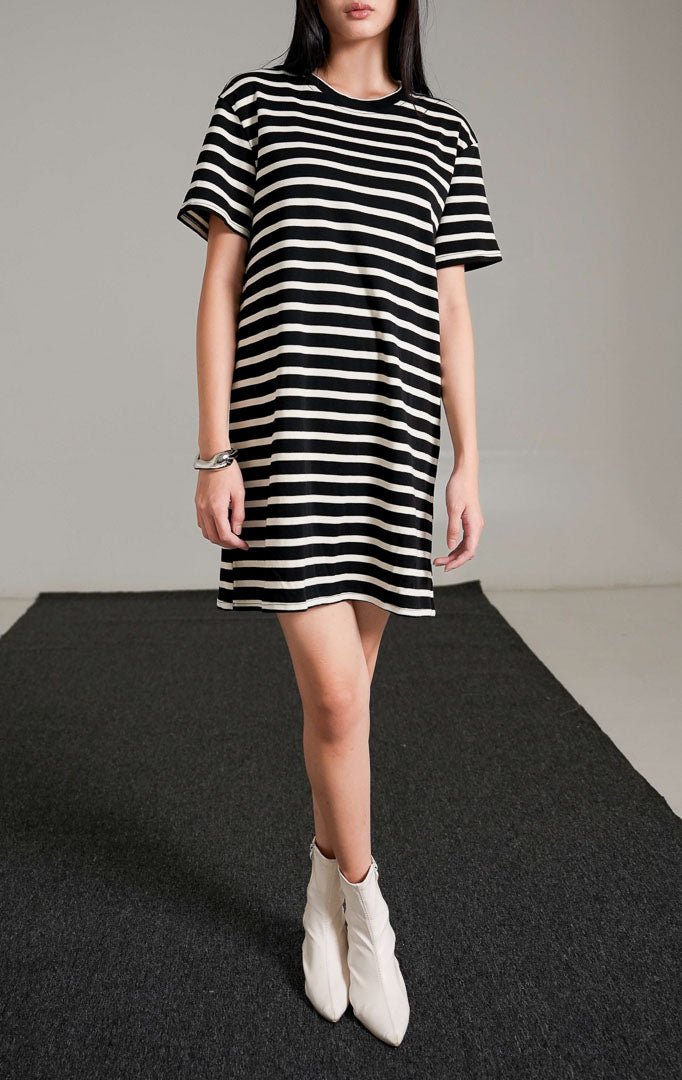 Breezy Striped Knit Dress, sebuah t-shirt dress pendek lengan pendek bermotif garis horizontal hitam dan putih, dipadukan dengan sepatu boots putih.