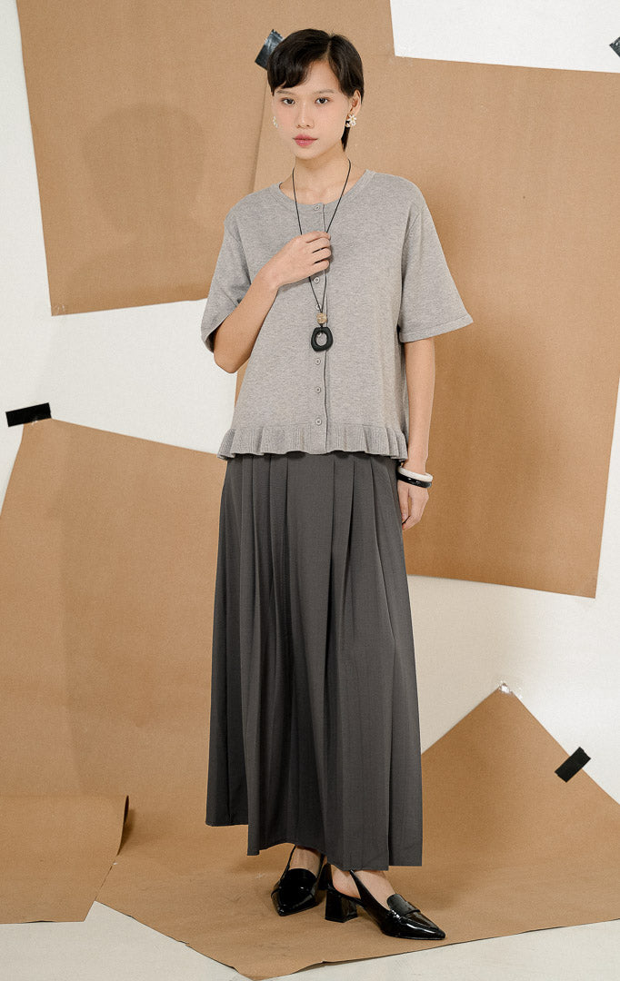 Model mengenakan Brinley Ruffle Hem Round Neck Top Grey, produk atasan rajut wanita lengan pendek warna abu-abu dengan kancing depan dan detail rempel.