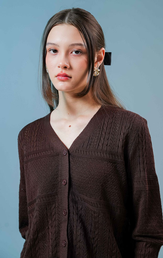 Model wanita mengenakan Wilder Cable Knit Pointelle Cardigan warna dark brown, luaran cardigan rajut wanita leher V-neck berwarna coklat tua dengan perpaduan motif rajut kepang dan lubang mikro anggun.